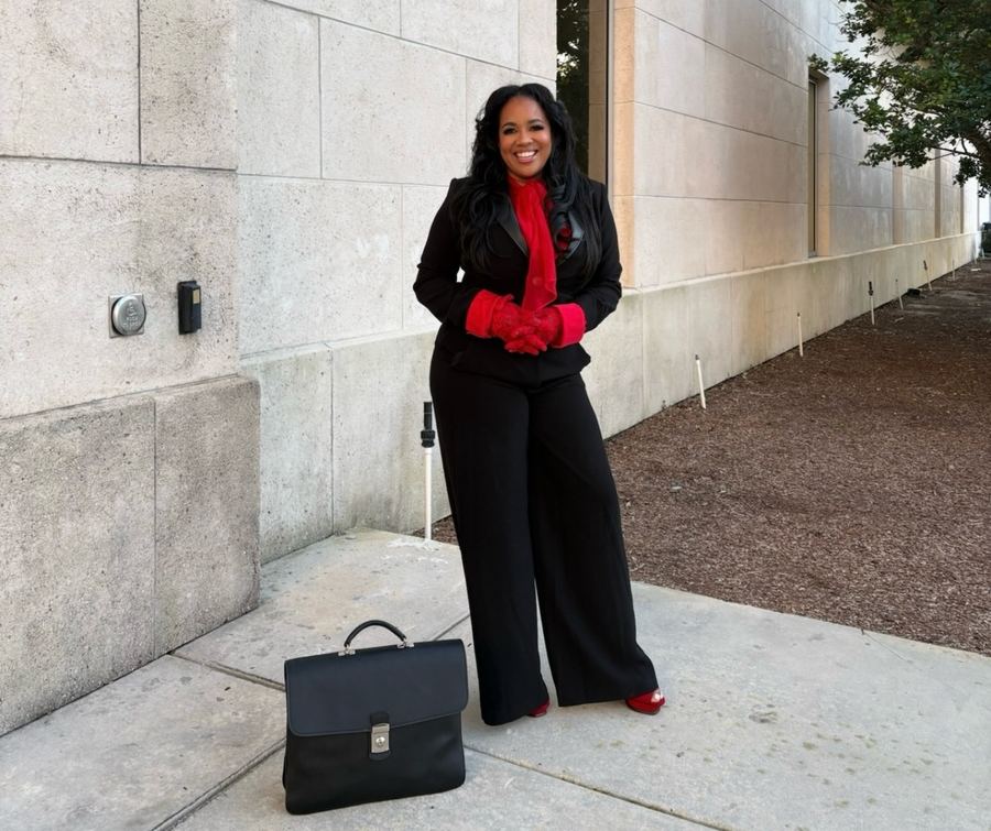 Lahteefah Parramore in a black suit with red gloves, carrying a briefcase